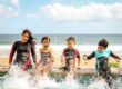 Travel insurance coverage - four happy children in wetsuits splashing in the sea